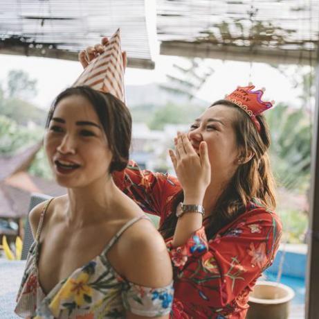 ett uppriktigt ögonblick där en asiatisk kinesisk kvinna hjälper sin syster att knyta upp festhatten och gör sig redo för födelsedagsfirandet