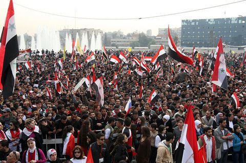 Syriska regimens anhängare vinkar med sin nationella flagga när de firar avslöjandet av statyn "Syrian Soldier" under ett sammanträde i Damaskus den 21 december 2011.