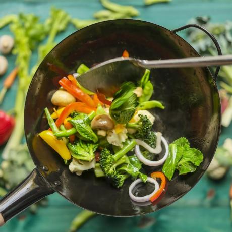 wok och fräs en mängd färska färgglada marknadsgrönsaker i en varm ångande wok med grönsaker på på en turkosfärgad träbordsbakgrund under woken